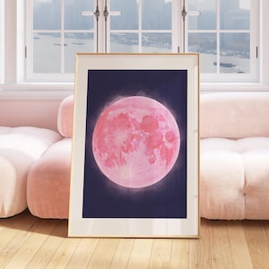 Peut inclure: Une impression encadrée d'une lune rose sur un fond bleu foncé. La lune est pleine et a une surface texturée. Le cadre est doré.