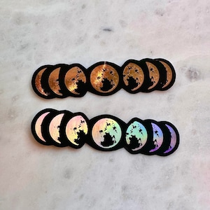 以下が含まれることがあります： 月の満ち欠けのステッカーが2列並んでいます。上の列は金色で、下の列は虹色です。