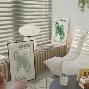 May include: A room interior featuring two framed zodiac art prints, "Aquarius" and "Capricorn", with abstract designs in pastel colors. A white lamp, a record player, and a modern white sofa are also visible. The room has a minimalist aesthetic.