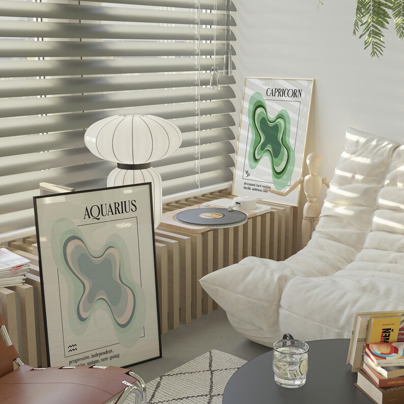 May include: A room interior featuring two framed zodiac art prints, "Aquarius" and "Capricorn", with abstract designs in pastel colors. A white lamp, a record player, and a modern white sofa are also visible. The room has a minimalist aesthetic.