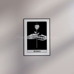 Puede incluir: Ilustraci&oacute;n de carta de tarot en blanco y negro de la carta de Los Enamorados. Dos manos esquel&eacute;ticas sostienen una sola rosa blanca con un tallo negro. La carta est&aacute; enmarcada en negro y tiene el texto "the lovers" en la parte inferior.