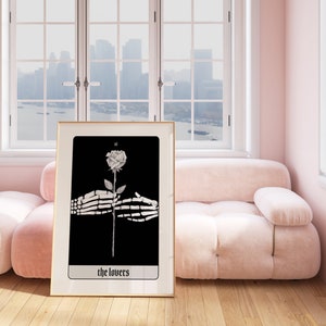 Puede incluir: Una ilustraci&oacute;n en blanco y negro enmarcada de una rosa sostenida por dos manos esquel&eacute;ticas. La carta se titula "The Lovers" y forma parte de una baraja de tarot.