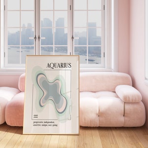May include: A framed art print featuring the word "AQUARIUS" in black font, with a colorful abstract design in shades of green, gray, and pink. The print includes the words "progressive, independent, assertive, unique, easy going". The print is displayed in a room with a pink sofa.