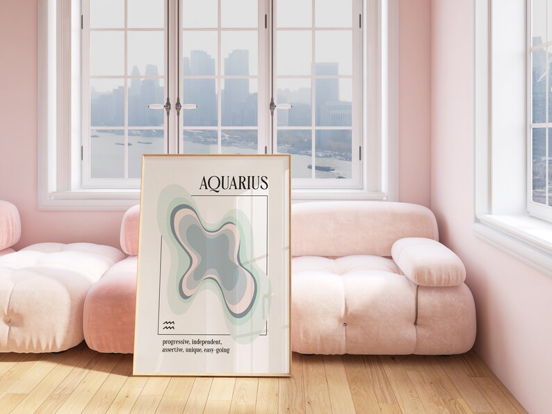 May include: A framed art print featuring the word "AQUARIUS" in black font, with a colorful abstract design in shades of green, gray, and pink. The print includes the words "progressive, independent, assertive, unique, easy going". The print is displayed in a room with a pink sofa.