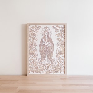 Op de afbeelding: Een ingelijste prent met een religieuze afbeelding van een vrouw die een kind vasthoudt, omringd door sierlijke bloemen- en krulwerkontwerpen. Het kunstwerk is uitgevoerd in beige- en bruintinten, met een ster boven het hoofd van de vrouw. De lijst is licht van kleur.
