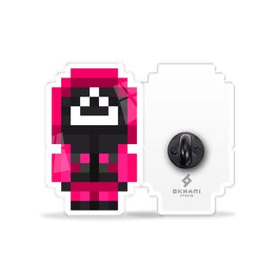 Könnte beinhalten: Eine pinkfarbene und schwarze Pixelfigur mit einem weißen Gesicht und einem schwarzen Lächeln. Die Figur trägt einen pinkfarbenen Hoodie und eine schwarze Hose. Die Figur befindet sich auf einem weißen Hintergrund mit einem schwarzen Nadelrücken.