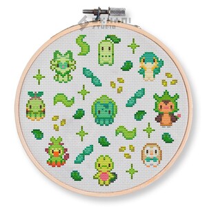 May include: A round embroidery hoop with a white fabric background featuring a pattern of green and yellow pixelated characters and leaves. The characters are inspired by popular video game characters.