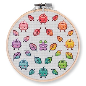 Puede incluir: Un patrón de punto de cruz que presenta un círculo de manzanas coloridas con caras sonrientes y hojas. Las manzanas están dispuestas en un patrón de arcoíris, con manzanas rojas, naranjas, amarillas, verdes, azules, moradas y rosas.