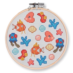 Puede incluir: Un aro de bordado redondo con fondo blanco y un diseño de punto de cruz colorido. El diseño presenta peces, conchas, corales y estrellas de mar.