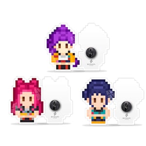 May include: Three pixel art character enamel pins with black pin backs. The characters have purple, pink, and blue hair, and are wearing colourful outfits. The pins are on white backing cards with the brand name "OKHARI" printed on them.