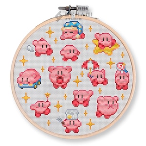 Puede incluir: Un aro de bordado de punto de cruz rosa y blanco con un patrón de varios personajes rosas de Kirby de la serie de videojuegos. Los personajes se representan en diferentes poses y expresiones, incluyendo a Kirby con un gorro de cocinero, un gorro para dormir y sosteniendo un paraguas.