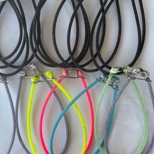 Pode incluir: Uma coleção de coleiras para cães em várias cores. As coleiras são feitas de corda e apresentam um laço de metal para prender uma trela. As cores incluem preto, cinza, amarelo neon, rosa, azul e verde. As coleiras estão dispostas em fileiras.