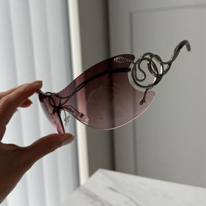 May include: A pair of sunglasses with a silver snake design on the frame. The lenses are a gradient of pink and purple.