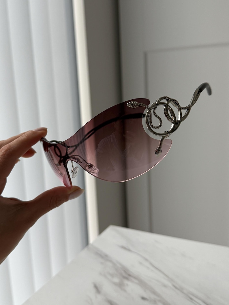 May include: A pair of sunglasses with a silver snake design on the frame. The lenses are a gradient of pink and purple.
