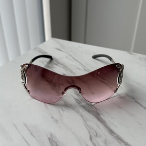 May include: A pair of pink tinted sunglasses with silver accents and a decorative design on the arms.