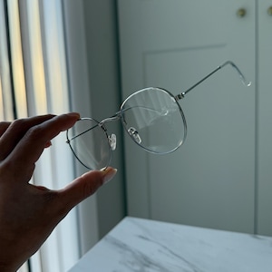 May include: Silver round frame eyeglasses with clear lenses.
