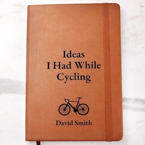 May include: Brown leather journal with the text "Ideas I Had While Cycling" and a silhouette of a bicycle. The name "David Smith" is printed below the bicycle.