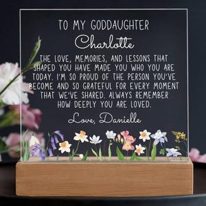 May include: A clear acrylic plaque with the text "TO MY GODDAUGHTER Charlotte" and a heartfelt message. The plaque sits on a wooden base and features a floral design at the bottom. The message is signed "Love, Danielle."