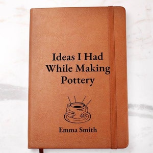 May include: A brown leather-bound journal with the text "Ideas I Had While Making Pottery" and a drawing of hands forming a clay pot. The journal is personalized with the name "Emma Smith".