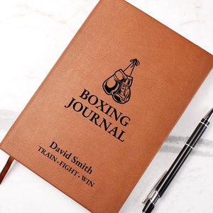May include: Brown leather-bound journal with the words "Boxing Journal" and "Train. Fight. Win."  The journal has a black illustration of boxing gloves and the name "David Smith" is engraved on the front.