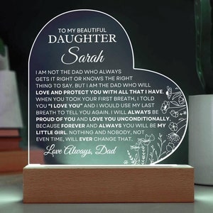 May include: A heart-shaped acrylic plaque with a wooden base, featuring the printed text: TO MY BEAUTIFUL DAUGHTER Sarah, followed by a heartfelt message from a father, and decorated with white line-art floral illustrations on the right side.
