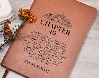 May include: A brown leather journal with the text "Chapter 40" and a floral design. The text below reads "Embrace the chapters you've written, for they have shaped you into the person you are today. With wisdom that guides you, may the love, memories, and you step into your next chapter with pride for all you have been, and with possibility for all you are yet to be." The name "Emma Smith" is printed at the bottom.