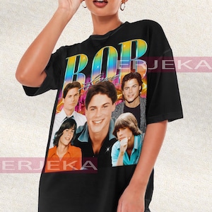 May include: Black unisex t-shirt featuring a colorful graphic of the word "BOB" and a collage of five men. The shirt is a vintage style, with a retro design. The model is wearing sunglasses.
