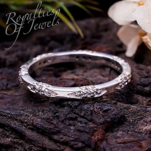 May include: A silver band ring with a delicate design of small diamonds set in a floral pattern. The ring is on a dark brown wooden surface.