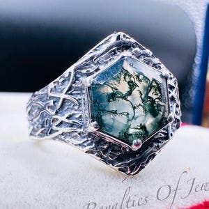 May include: A silver ring with a hexagonal green moss agate gemstone set in a textured silver band. The band has a tree-like design.