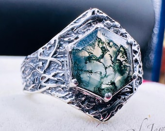 May include: A silver ring with a hexagonal green moss agate gemstone set in a textured silver band. The band has a tree-like design.