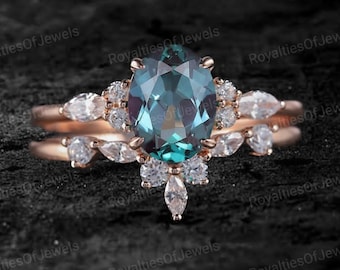 Può includere: Un anello di fidanzamento in oro rosa con una grande pietra preziosa verde di forma ovale circondata da piccole pietre bianche. L'anello è su uno sfondo nero.