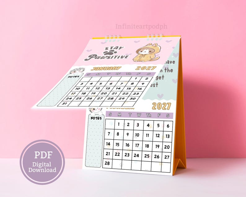 May include: A 2027 desk calendar with a spiral binding and a yellow stand. The pages feature a light pink background with a cartoon cat in a hoodie, the text Stay Pawsitive, and monthly grids for January and February with a notes section on the left.