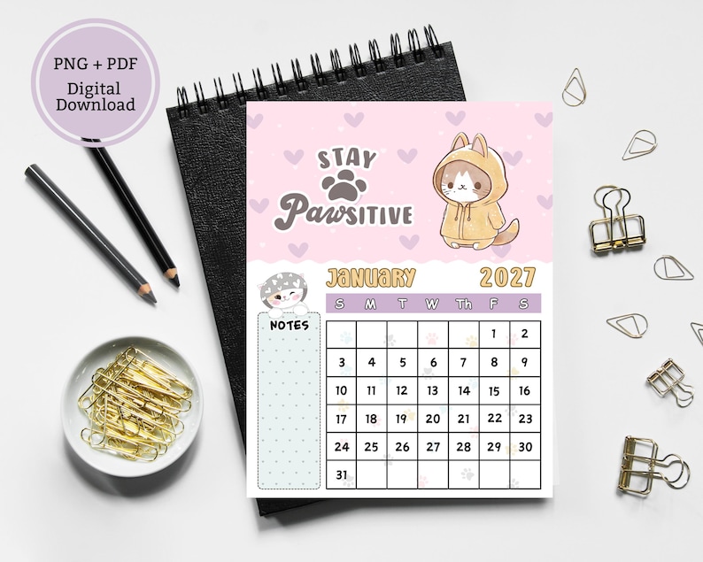 May include: A January 2027 calendar page featuring a light pink background with purple hearts, a cartoon cat in a yellow hoodie, and the text Stay Pawsitive. The calendar includes a grid for dates, a notes section, and a small cat illustration.