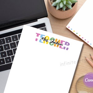 May include: A white notepad with the text "Teacher" in colorful letters and the name "Mrs. Jackson" written below. The notepad is on a wooden surface with a laptop, a potted plant, and two pencils.