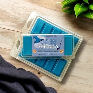 May include: Two blue wax melt snap bars in clear plastic packaging. The label reads "THINE CANDLES CO. GREY WIZARD leather | tobacco leaves | amber vegan wax blend 2 oz snap bar".