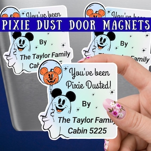 May include: Square magnets featuring a cartoon ghost with mouse ears holding an orange pumpkin balloon. The text reads You've been Pixie Dusted! By The Taylor Family Cabin 5225. The design includes small black star accents on a light blue and white gradient background.