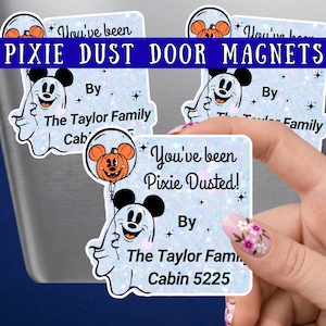 May include: Three square magnets with a light blue glitter background featuring a white ghost character holding an orange pumpkin balloon with mouse ears. The text reads You've been Pixie Dusted! By The Taylor Family Cabin 5225 with star accents.