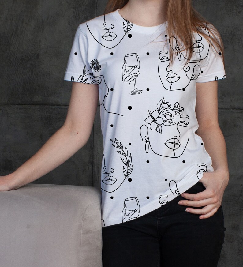 May include: White t-shirt with a black line drawing pattern of faces, flowers, and wine glasses. The pattern is repeated throughout the shirt.