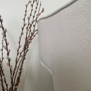 May include: A white, textured armchair with a curved back. A bouquet of white pussy willow branches with brown stems is in the foreground.