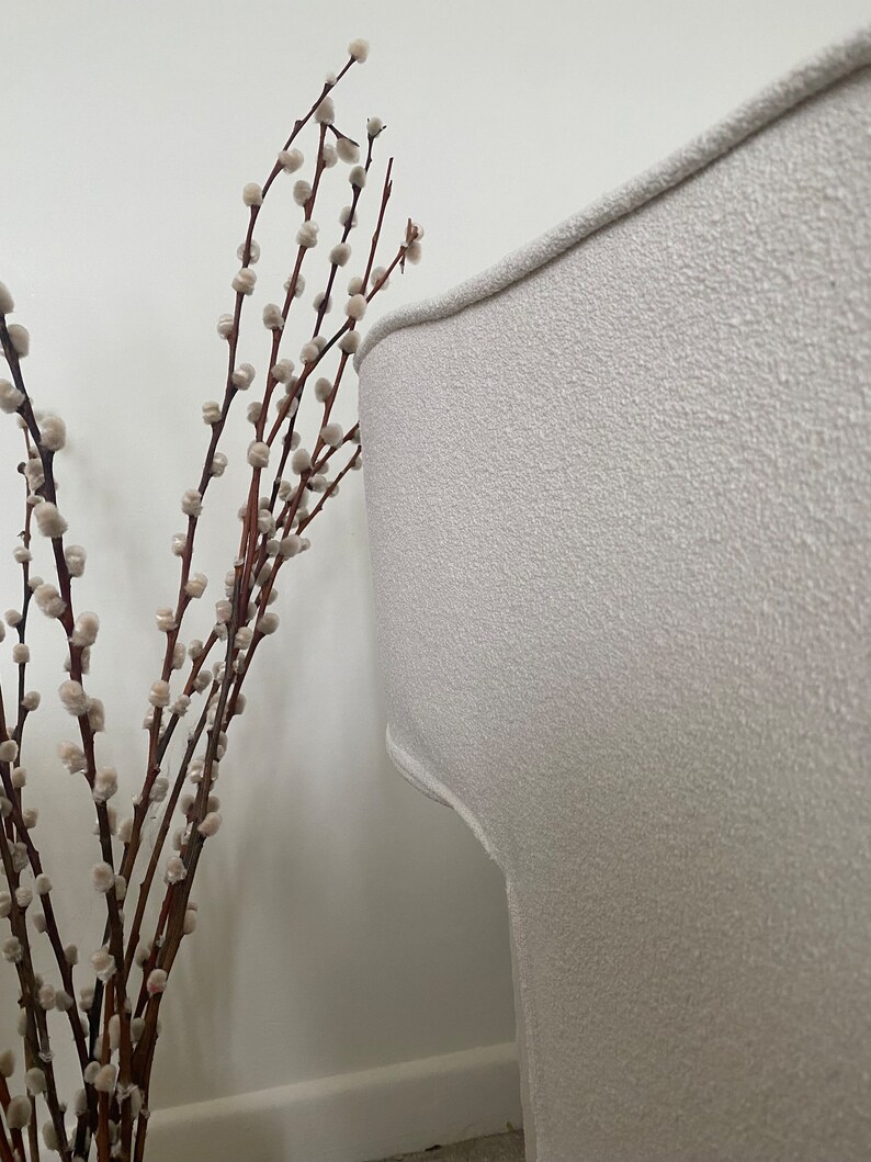 May include: A white, textured armchair with a curved back. A bouquet of white pussy willow branches with brown stems is in the foreground.
