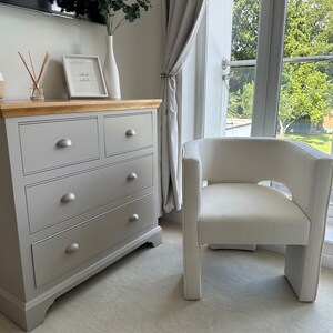 May include: A gray dresser with four drawers and a white chair with a white cushion. The chair is in front of a window with white curtains. The dresser has a sign on top that says "breathe in, exhale" in cursive.