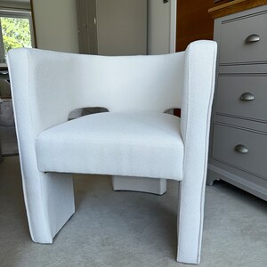 May include: A white upholstered armchair with a unique cutout design in the back. The chair has a simple, modern design and is perfect for a living room or bedroom.