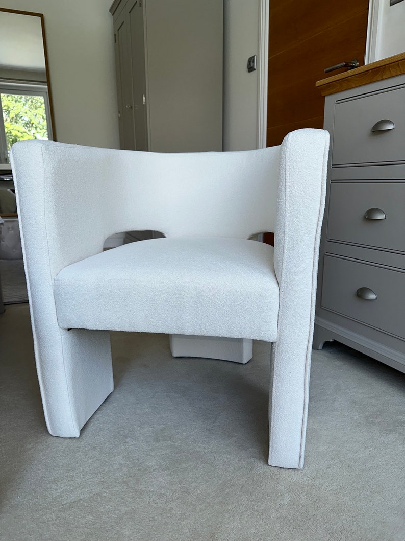 May include: A white upholstered armchair with a unique cutout design in the back. The chair has a simple, modern design and is perfect for a living room or bedroom.