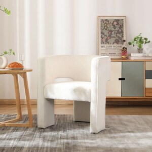 May include: A white upholstered armchair with a curved back and a wide seat. The chair is sitting on a gray rug in a room with white walls and a wooden floor.