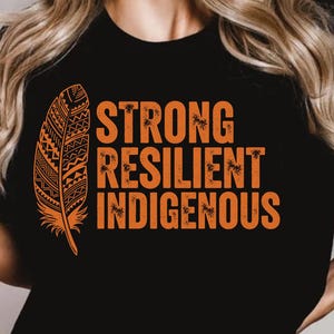 May include: Black t-shirt with the words "STRONG RESILIENT INDIGENOUS" in orange, along with an orange feather graphic. The shirt is worn by a person.