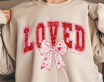 May include: A beige sweatshirt with a red glitter graphic that says "LOVED" with a pink bow and the text "John 3:16" underneath.