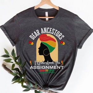 Może przedstawiać: Szary t-shirt z napisem "Dear Ancestors I Understood The Assignment Juneteenth" i sylwetką czarnej kobiety w kolorowym turbanie.