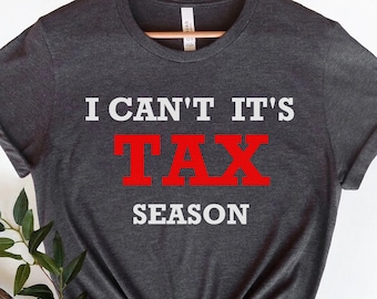 Könnte beinhalten: Ein dunkelgraues T-Shirt mit dem Text "I can't it's tax season" in weißer und roter Schrift.
