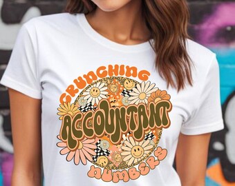 Könnte beinhalten: Weißes T-Shirt mit einem braunen und orangefarbenen Grafikdesign. Die Grafik zeigt den Text "Crunching Accountant Numbers" in einer Retro-Schriftart, umgeben von Blumen und Smiley-Gesichtern.