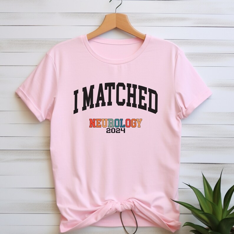 May include: Pink t-shirt with the text "I MATCHED NEUROLOGY 2024" in black and rainbow colours.